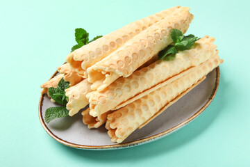 Plate with delicious wafer rolls and mint on turquoise background