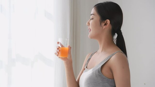 Holiday concept of 4k Resolution. Asian woman drinking orange juice after exercising at home.