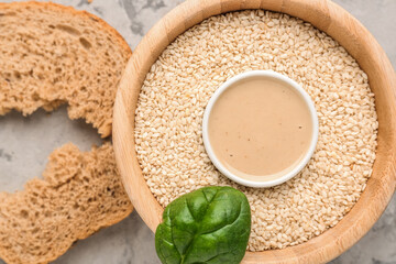 Composition with bowl of sesame seeds, tahini, bread and spinach on grunge background, closeup