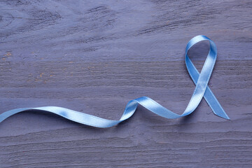 Blue awareness ribbon on dark wooden background. Prostate cancer concept