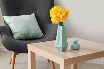 Vase with narcissus flowers and perfume on table in living room
