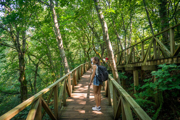 Woman Hiker with Backpack and Shorts Walking Up a Wooden Bridge in the Redwood Forest of Cabezon de la Sal in Santander, Spain