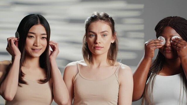 Models doing three wise monkeys sign with cotton pads on camera, being natural with radiant glowing skin. Young diverse girl promoting cleansing and cosmetology for skincare ad.