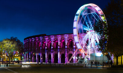 Spinning ferris wheel with motion blur near illuminated Arena of Nimes, France