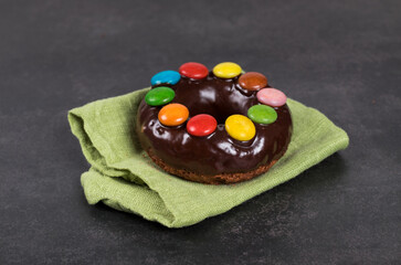 Easter Chocolate donut with chocolate glaze and decorated with colorful dragees. On a green linen napkin. Dark gray background. Bright Easter Holiday