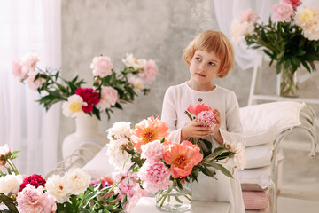 Child Blonde 6-7 years old in a white dress holds pale pink flowers in her hand. The concept of congratulations on March 8, flower shop or greenhouse, botanical garden or environmental protection.
