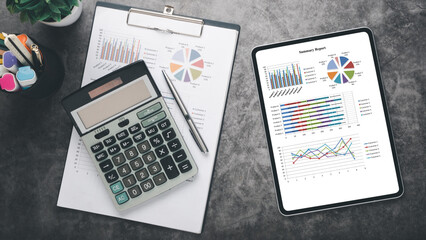 Obraz premium Tablet with charts and reports on office desk workplace. Top view flat lay.