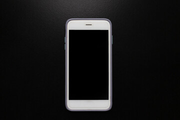 Mobile phone with black blank screen on black background with light from above.
