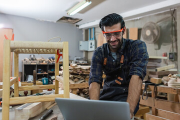 young carpenter caucasian man with laptop make drawing on wood to design at workspace. craftsman...