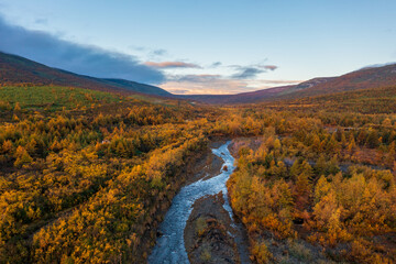 Beautiful autumn landscape. Aerial view of a river in a mountain valley. Trees and bushes with...