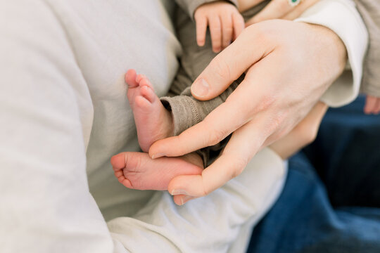 A parent holds their newborn baby in their hands. You can see newborn baby feet and a hand in this photo. 