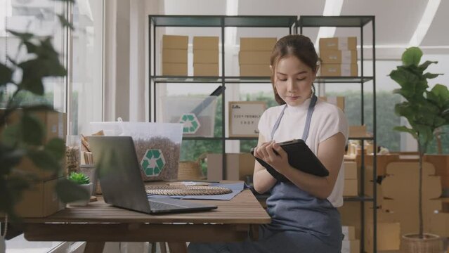 Cloud ERP martech for smart SME. Go green vendor net zero ESG store using easy CRM social media platform on tablet laptop at office. Young adult seller woman asia people happy work at retail box shop.