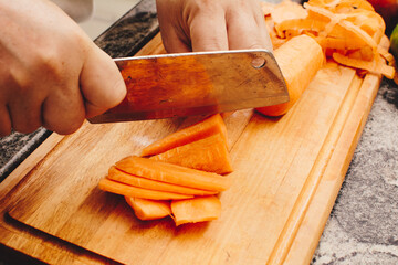 Woman slicing carrots on bamboo cutting board on granite kitchen countertop