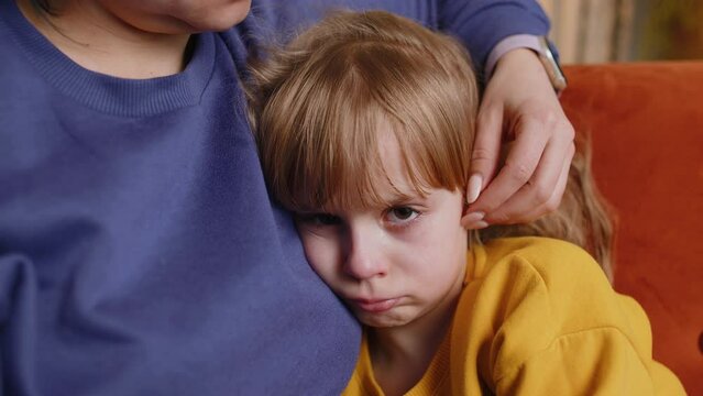 Close-up of sad girl kid is crying and lying on mother at home. Violence against children in family. Quarrel, bullying at school. Child toddler abuse. Mom hugs, embrace, takes pity on her daughter