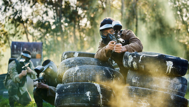 Team, paintball and tires for cover bunker or protection while firing or aiming down sights together in nature. Group of people waiting in teamwork for opportunity to attack or shoot in extreme sport