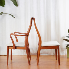 Mid-century modern wooden dining room chairs. Back-to-back view in front of long white curtains with houseplants. 