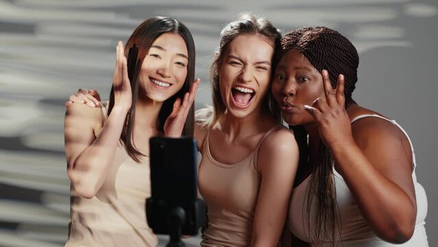 Interracial group of friends taking photos on smartphone to promote self acceptance and body positivity. Women laughing and acting funny on pictures, enjoying skincare ad campaign.