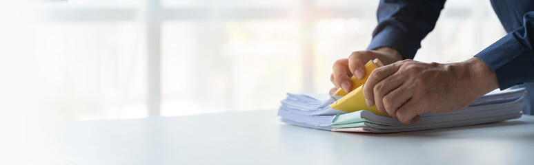copy space of young businessman searching piles of documents on his desk for financial report paper...
