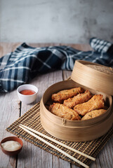 dim sum dumplings in bamboo steamer with sauce on wood table