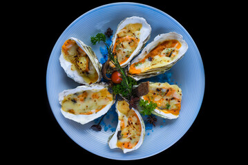 oysters baked with cheese on plate with blue salt isolated on black side view