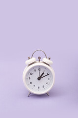 Reloj despertador color blanco ilustrando cambio de horario primavera, verano sobre fondo morado