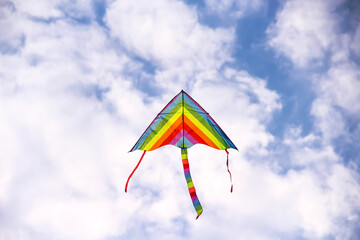 Kite in hand flying on bright blue sky white clouds background