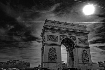 Fototapeta premium Arc de Triomphe and dramatic cloudscape with the bright sun in Paris, France, monochromatic high contrast black and white photography
