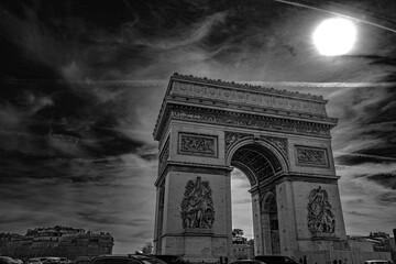Arc de Triomphe and dramatic cloudscape with the bright sun in Paris, France, monochromatic high...