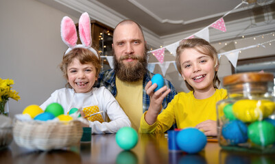 Easter Family traditions. Father and two caucasian happy children with bunny ears dye and decorate...