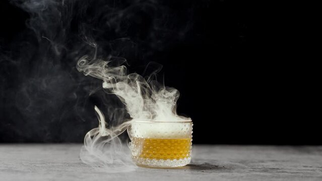 Smoke rolling off of a cocktail with a black background.