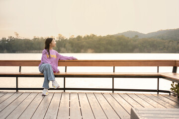 Fototapeta na wymiar Asian girl sitting and enjoying the morning scenery by the lake with mountains