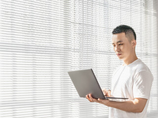 Asian man is using laptop near the window.