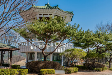 Three story white pagoda under blue sky in roadside park.