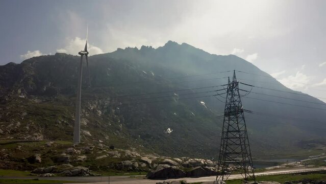 Aerial view: Wind mill and electricity cables against mountain background. Drone shot