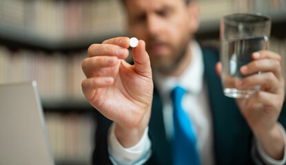 Close up portrait of man taking a medicine pill from headache migraine. Hand with medicine pill selective focus. Tired man suffering from headache after computer work.