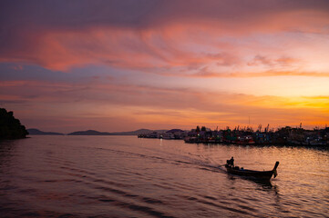 Stunning colorful sunset sky with traditional longtail boat speeding at fisherman village in phuket, Thailand.