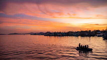 Stunning colorful sunset sky with dinghy boat speeding at fisherman village in phuket, Thailand.