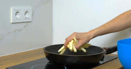 Woman prepared french fries for cooking on frying pan. Putting potatoes on pan