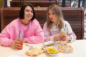 Two women friends eating, smiling and talking in cafe