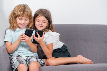 Children alone with phone at home. Sibling kids using smartphone together. Children playing game on mobile phone, watching online content on internet. Gadget addiction. Mobile addict concept.