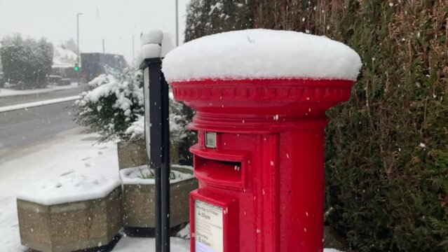 A classic British red pillar postbox near a lampost in the snow at christmas.