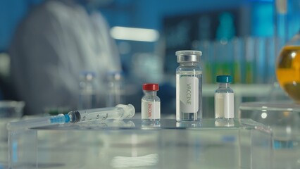 Glass vials with a vaccine and a syringe on a blurred laboratory background. Bottles with clear liquid and light reflection. Medical background, close up.