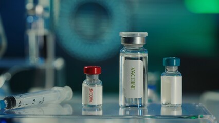 Glass vials with a vaccine and a syringe on a blurred laboratory background. Bottles with clear...