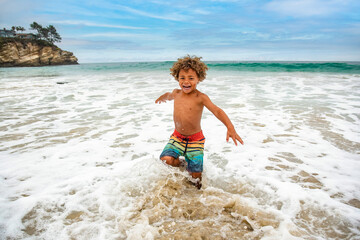 Smiling young African American boy running and playing at the beach while on a family vacation. Playing in the ocean waves having fun and being active