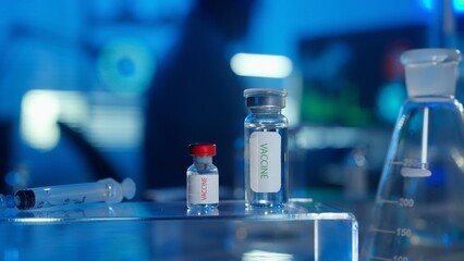 Glass vials with a vaccine and a syringe on a blurred laboratory background in blue light. Bottles with transparent liquid and light reflection. The concept of vaccination. Close up.