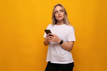 a woman in a white T-shirt with a smartphone in her hands uses an application on a yellow background