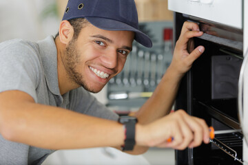 handsome young repairman fixing oven with screwdriver