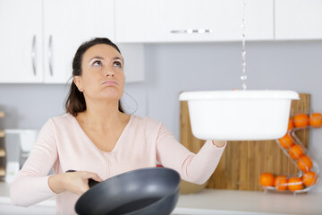 worried woman holding bucket while water droplets leak from ceiling