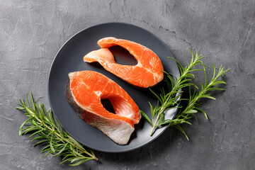 Steak of fresh raw red fish salmon with lemon, rosemary and pepper on black background