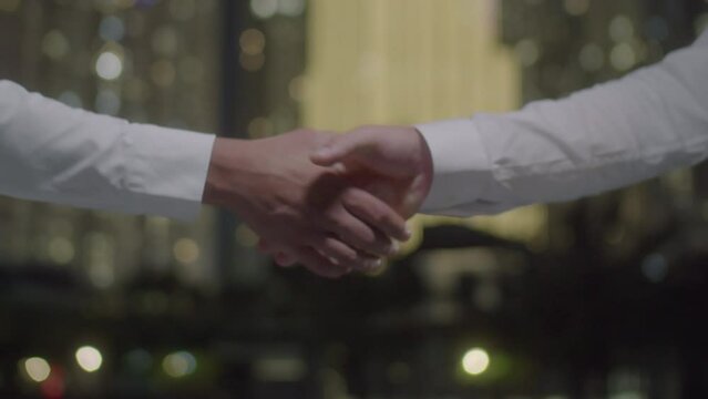 Cropped shot of handshake of two unrecognizable business partners in formalwear outdoors in night city